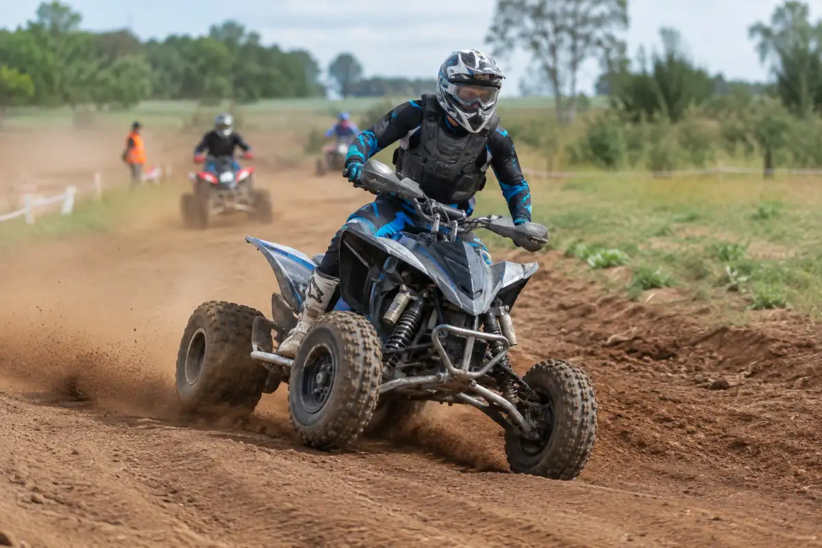 Pilote équipé en quad sportif qui négocie un virage sur un circuit de terre lors d’une course d’endurance quad.