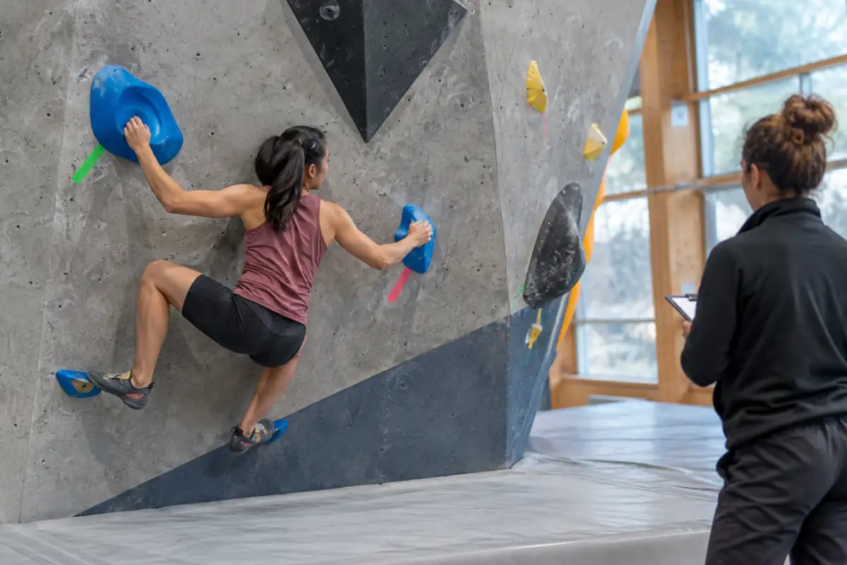 Départ d’un bloc en compétition : mains sur les prises marquées, pieds en position et tapis dégagé sous le grimpeur.