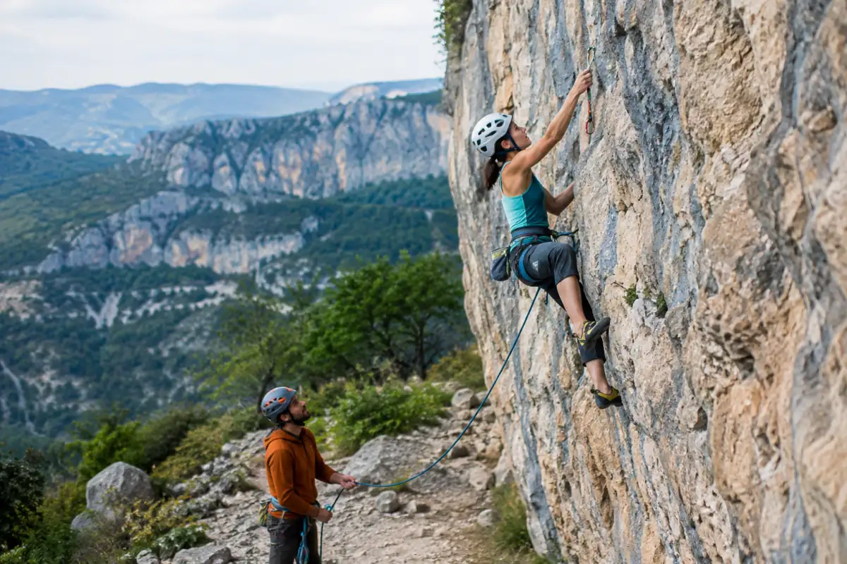 Une grimpeuse progresse en tête sur une voie équipée, assurée par son partenaire au pied d’une falaise calcaire française.