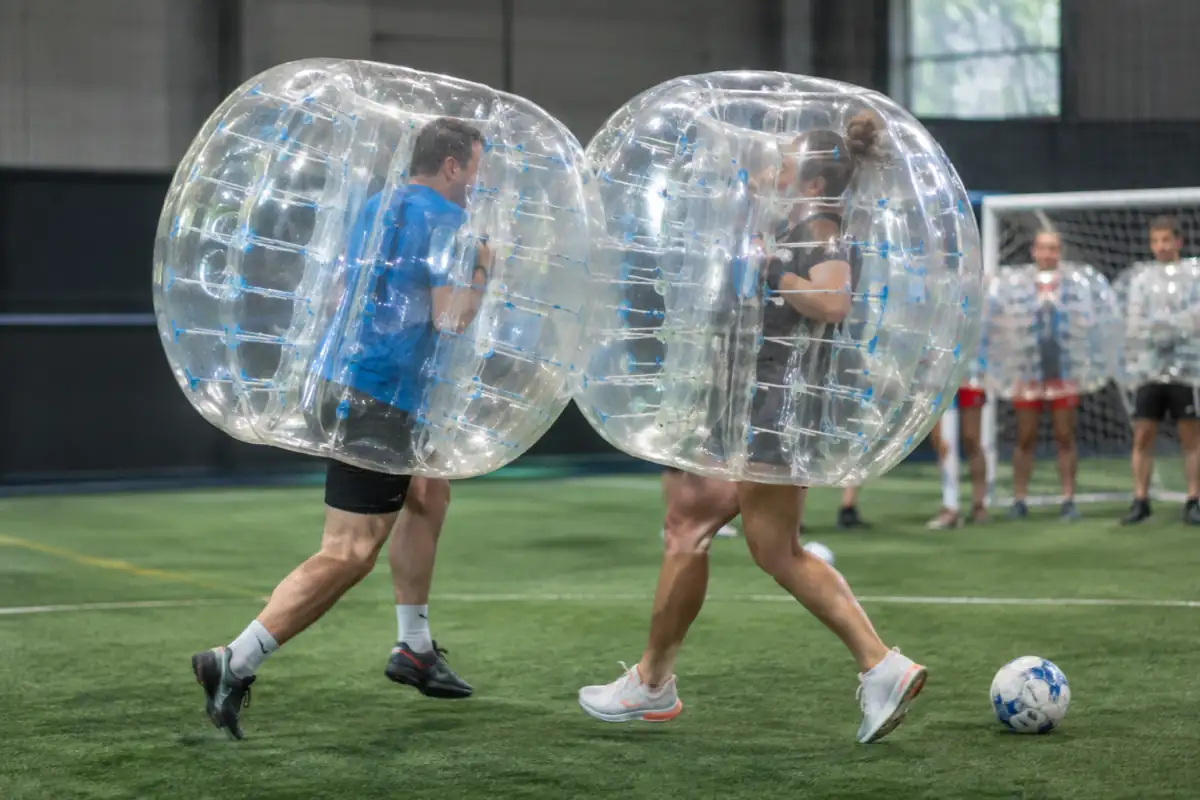 Deux joueurs en bulles gonflables se disputent le ballon lors d’une partie de football en bulle sur un terrain intérieur.