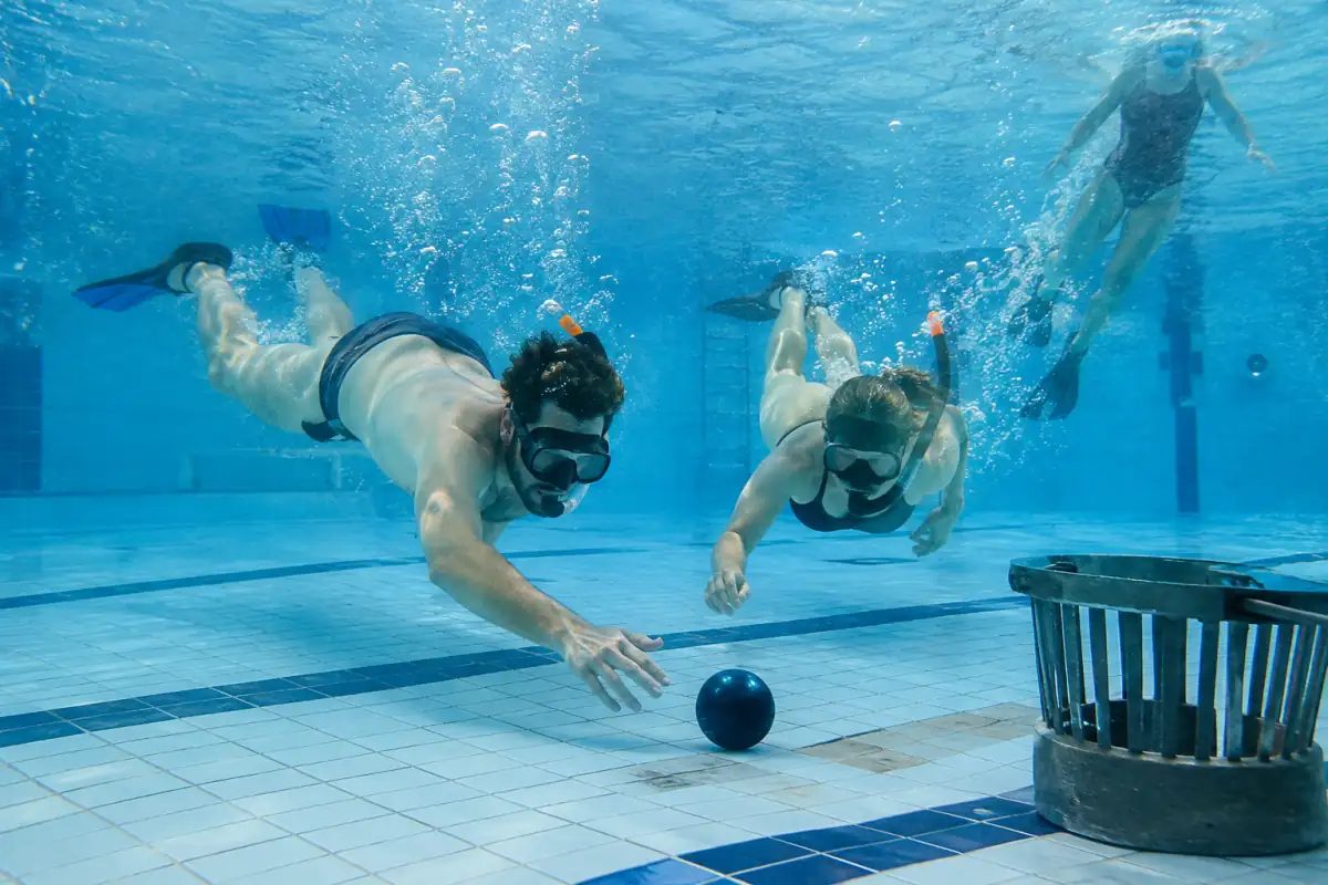 Des joueurs en masque et palmes se disputent un ballon lesté près d’un but au fond d’une piscine.