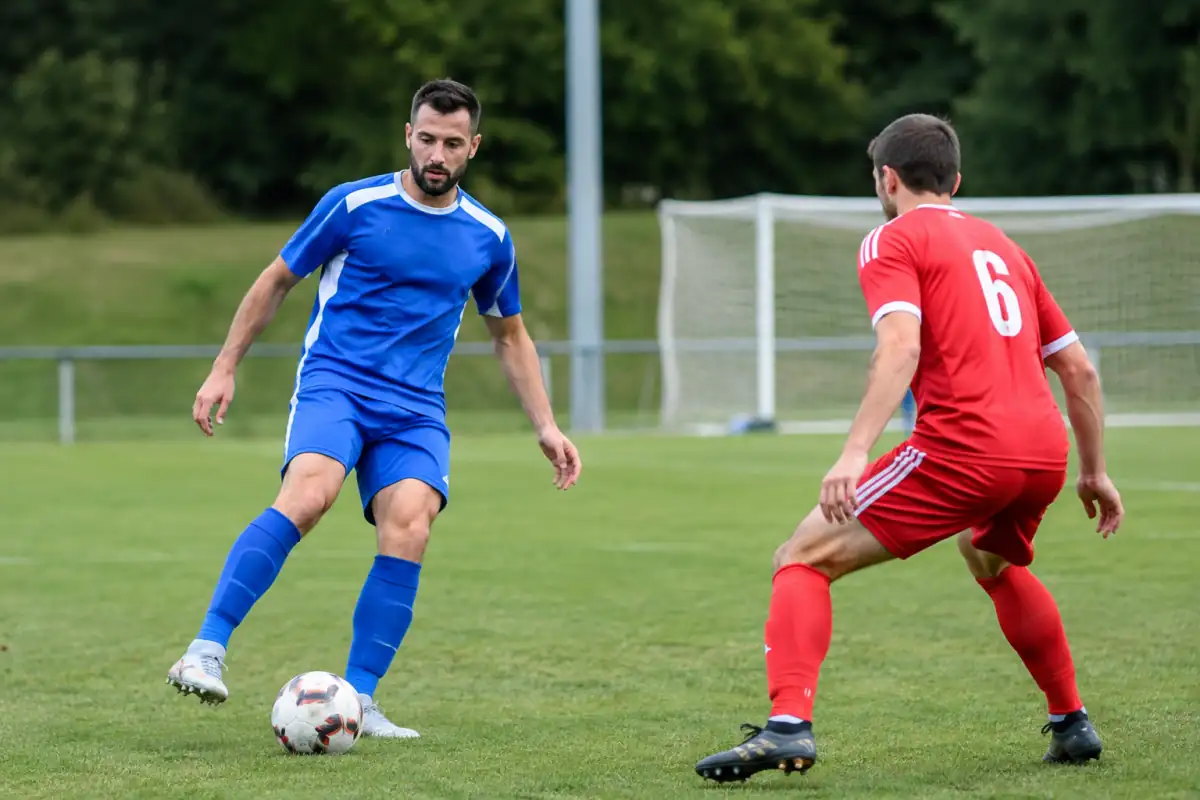 Deux joueurs disputent le ballon sur un terrain de gazon lors d’un match amateur de football en France.