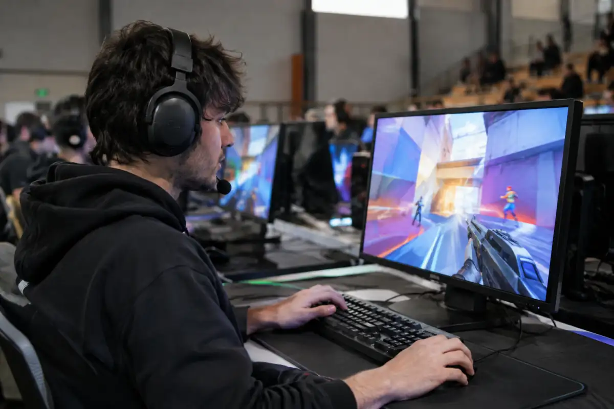 Un joueur de FPS d’arène participe à une compétition sur ordinateur, clavier, souris et casque dans une salle de jeu.