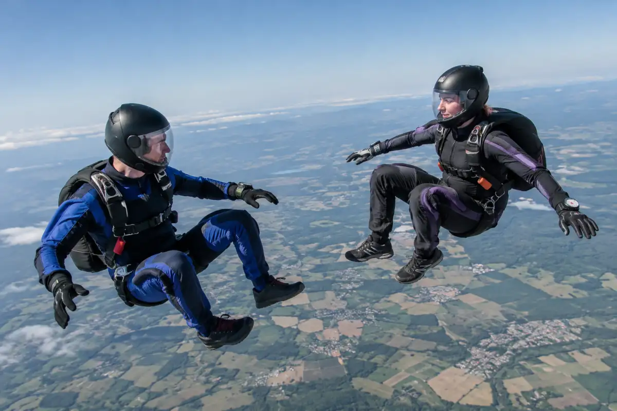 Deux parachutistes en combinaison de freefly maintiennent une position assise contrôlée en chute libre au-dessus d’un centre français.