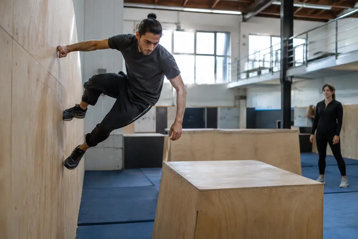 Une pratiquante de freerunning franchit un module bas et prépare une réception contrôlée dans une salle d’entraînement.