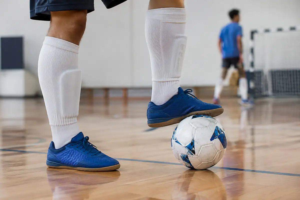 Chaussures indoor à semelle plate contrôlant un ballon de futsal taille 4 sur le parquet d’un gymnase.