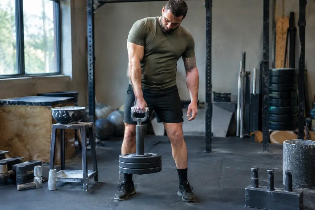 Athlète réalisant un levage au rolling handle lors d’une séance de grip sport en salle, avec disques et magnésie.