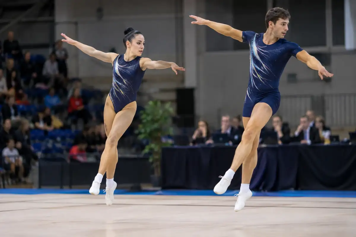 Deux gymnastes exécutent un saut synchronisé de gymnastique aérobic sur le praticable lors d’une compétition en salle.