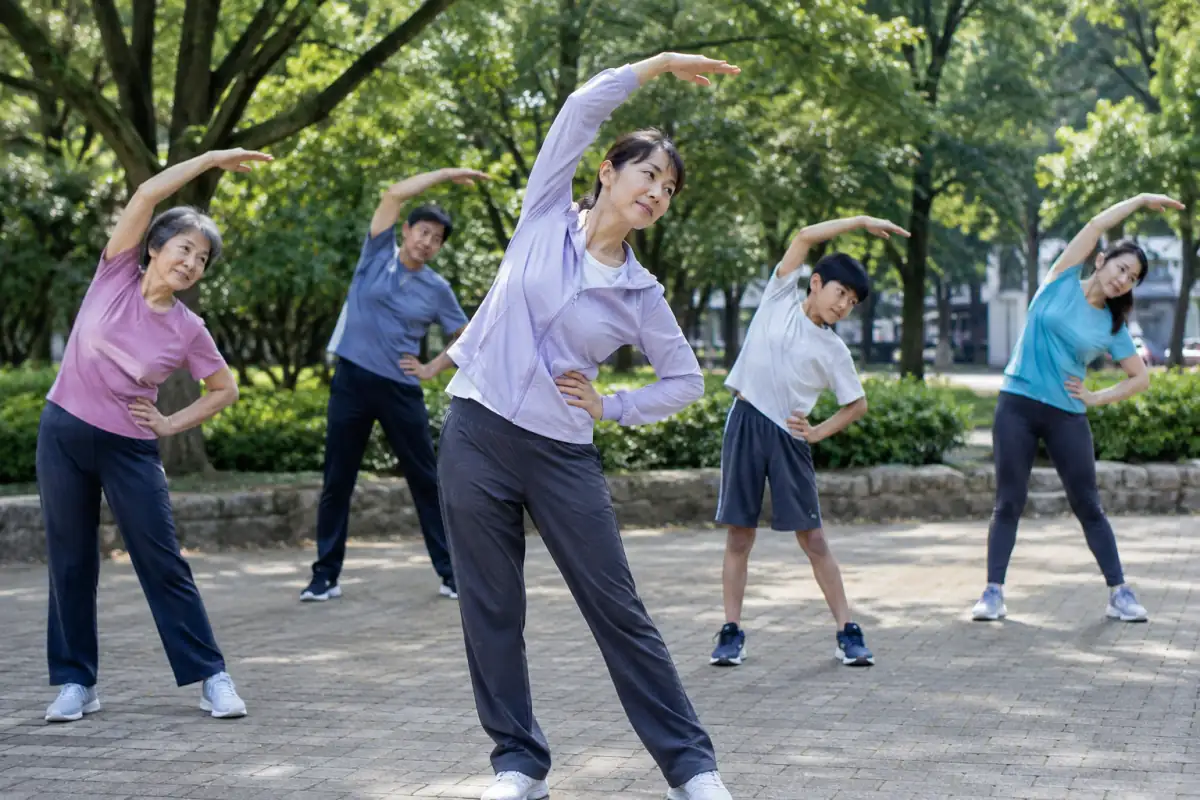 Un groupe pratique le rajio taisō dans un parc, en réalisant ensemble un mouvement latéral d’extension des bras.