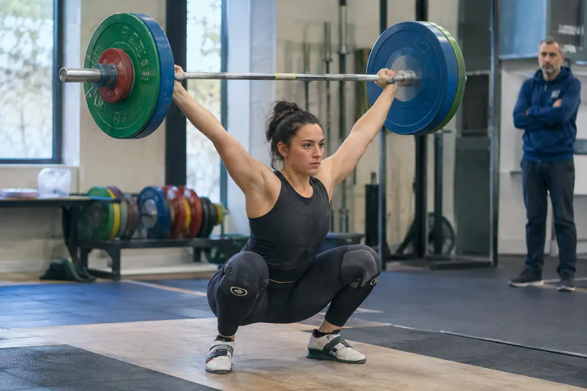 Haltérophile réalisant un arraché en réception au-dessus de la tête sur une plateforme de club.