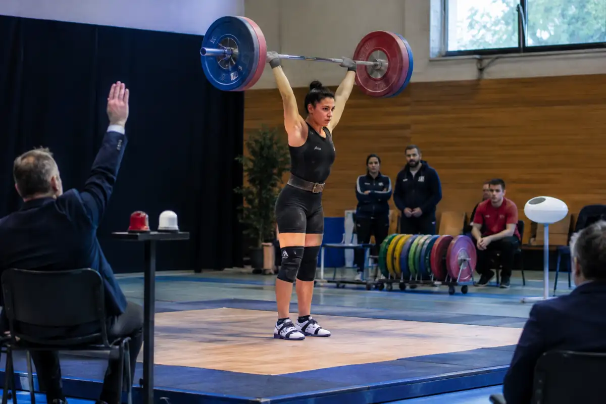 Haltérophile stabilisant la barre au-dessus de la tête sur le plateau, sous le regard des arbitres avant le signal de descente.
