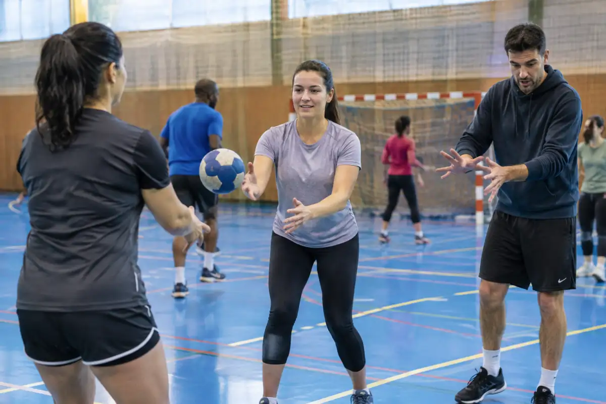 Une débutante adulte travaille la réception d’une passe avec un partenaire lors d’un entraînement loisir de handball en salle.