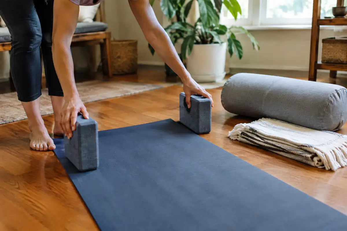 Tapis de yoga avec deux briques, une couverture pliée et un bolster préparés pour une séance de hatha yoga à domicile.