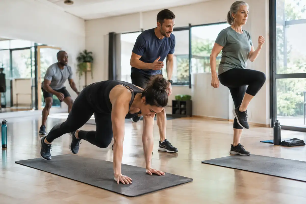 Séance de HIIT en salle : une pratiquante réalise un squat thrust pendant qu’un coach observe le mouvement.