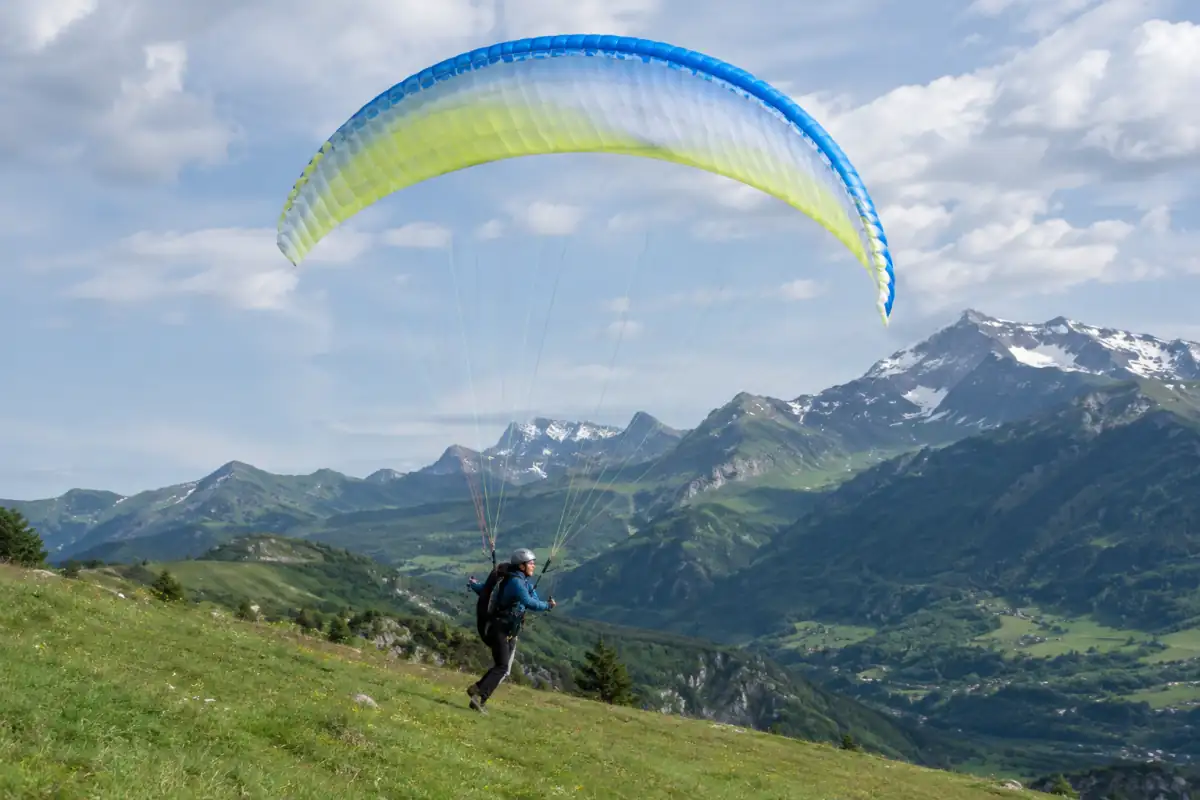Un pilote équipé pour le hike and fly décolle en parapente d’une pente herbeuse dans les Alpes françaises.