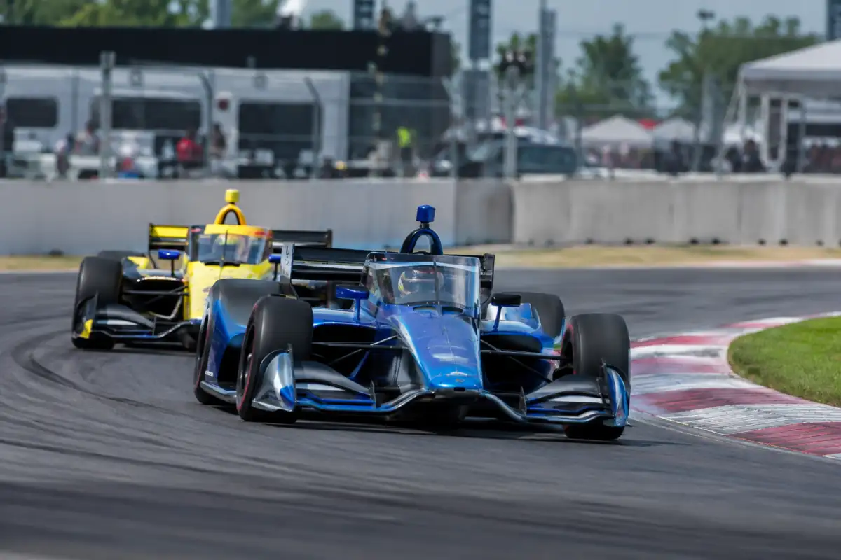 Des monoplaces d’IndyCar négocient un virage sur circuit, ailerons, pneus slicks et cockpit protégé visibles.