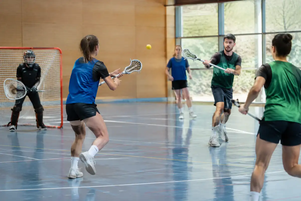 Des joueurs pratiquent l’intercrosse en salle, en se passant une balle souple avec des crosses à poche sans contact physique.