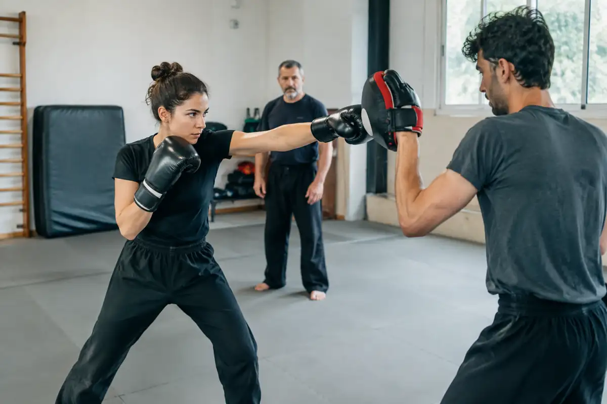 Deux pratiquants travaillent une frappe directe de jeet kune do sur des pattes d’ours dans une salle d’entraînement.