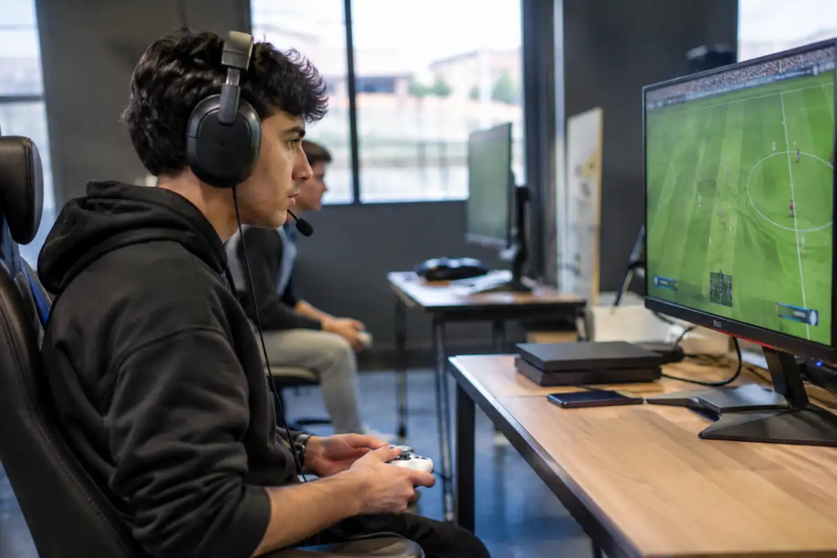 Joueur d’e-football concentré sur un match de simulation de football, manette en main, dans une salle de jeu.