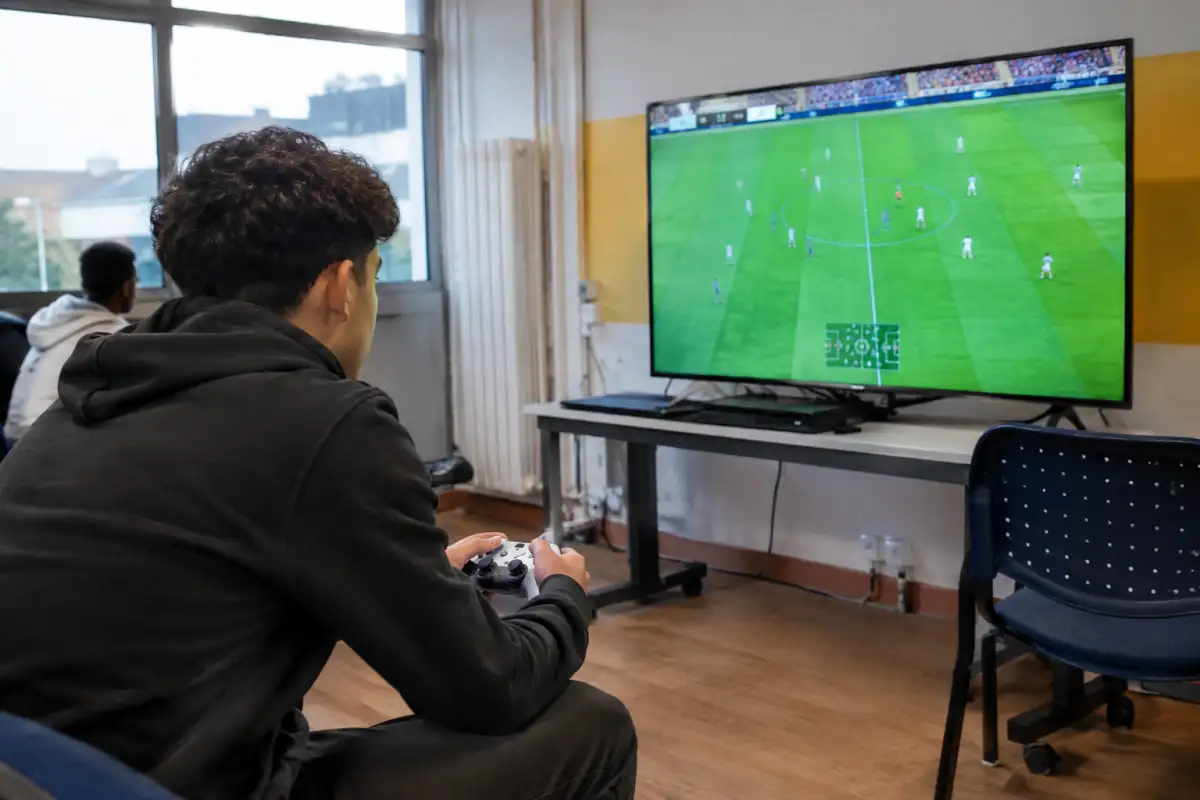 Débutant concentré sur un jeu de football avec une manette lors d’une séance dans une salle associative.