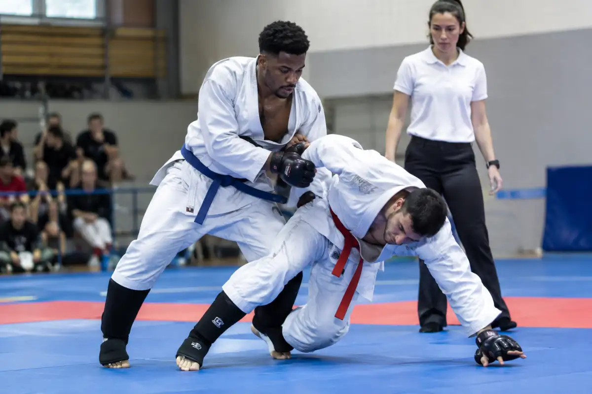 Deux combattants en kimono exécutent une saisie et une projection de ju-jitsu sportif sur un tatami en salle.