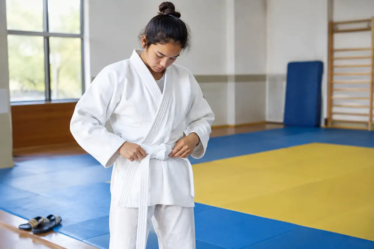 Judogi blanc ajusté près des poignets et des chevilles, avec une ceinture nouée sur un tatami de judo.