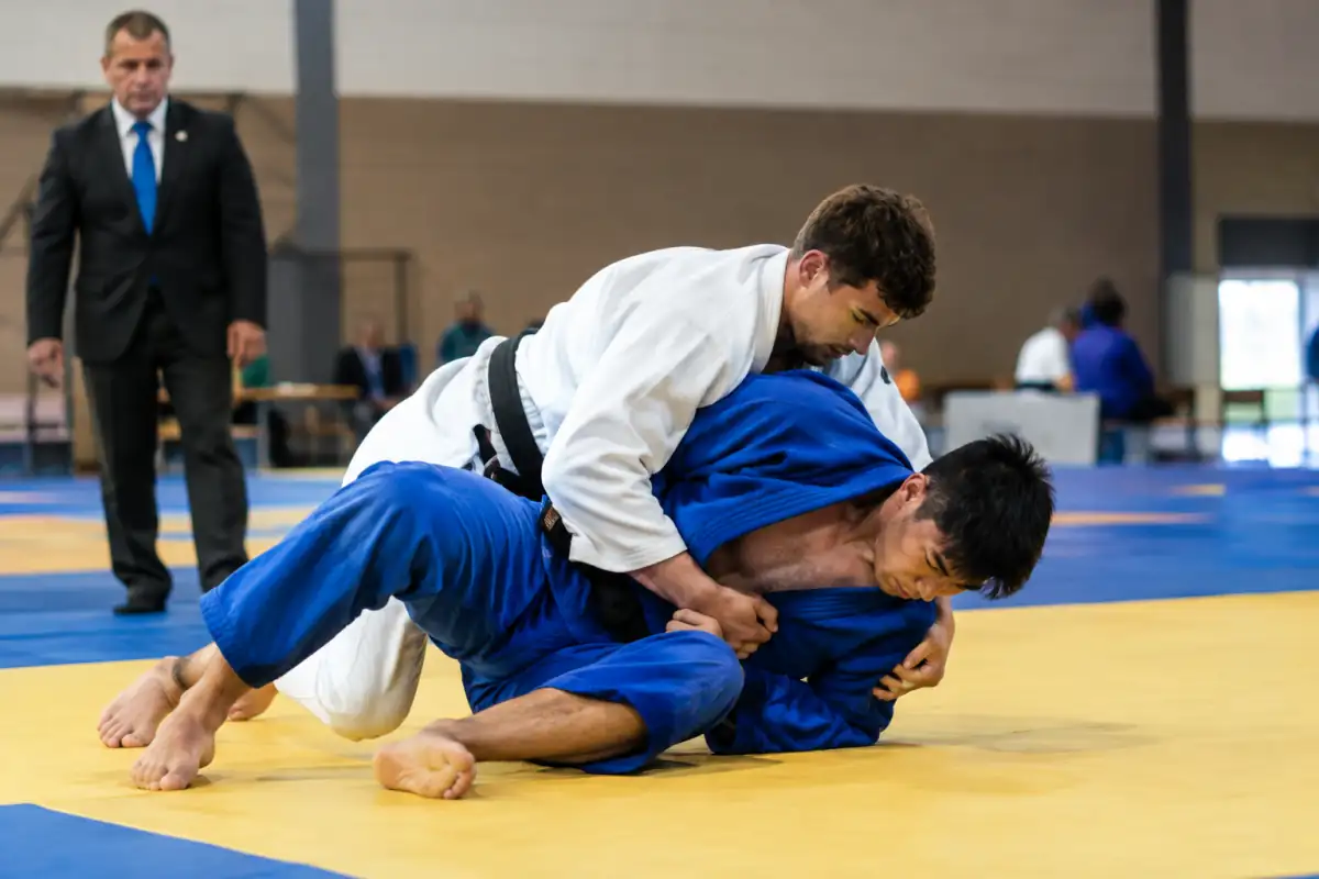 Un judoka contrôle son adversaire au sol pendant que celui-ci tente de sortir de l’immobilisation sur le tatami.