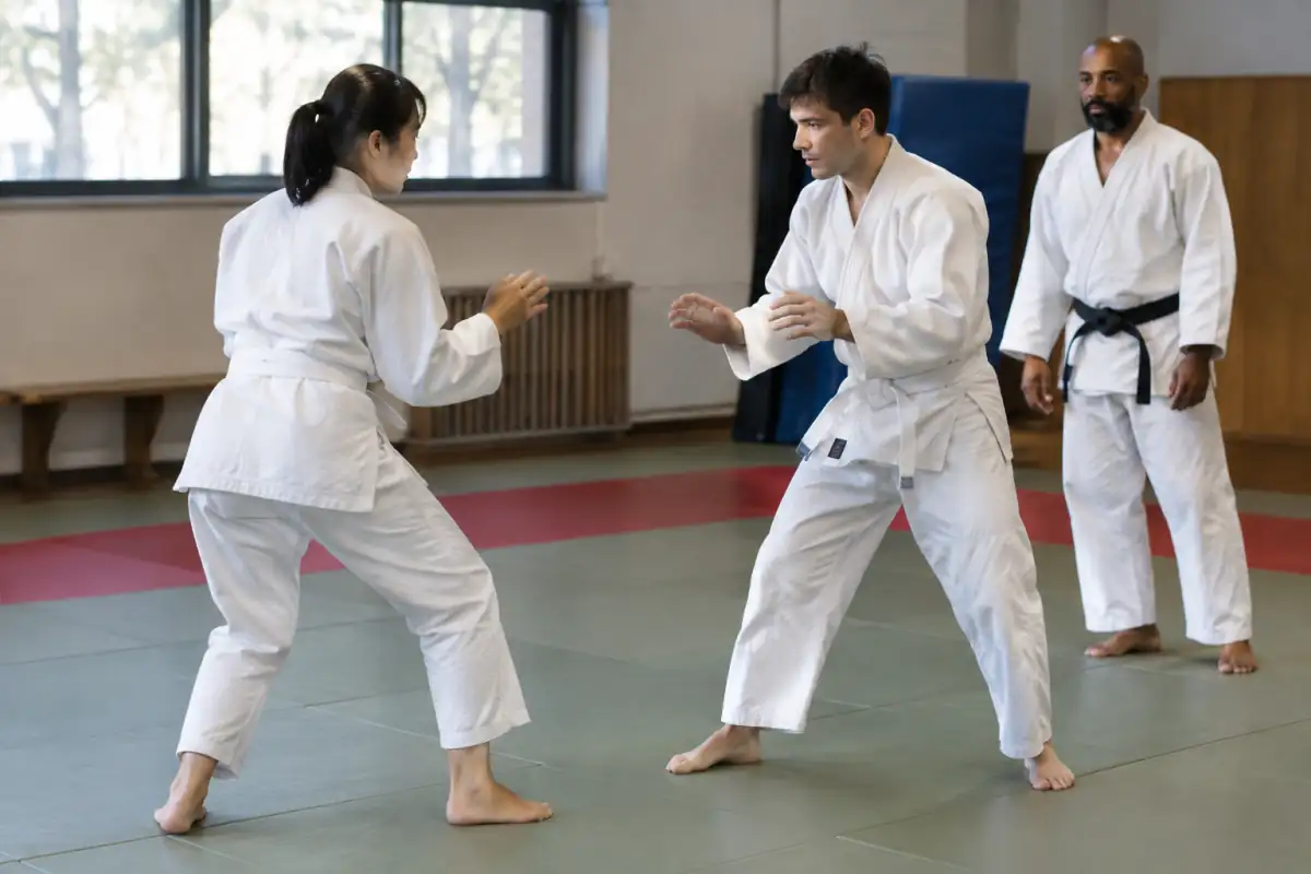 Deux débutants en jujitsu travaillent lentement leurs déplacements sur tatami sous le regard attentif d’un enseignant.