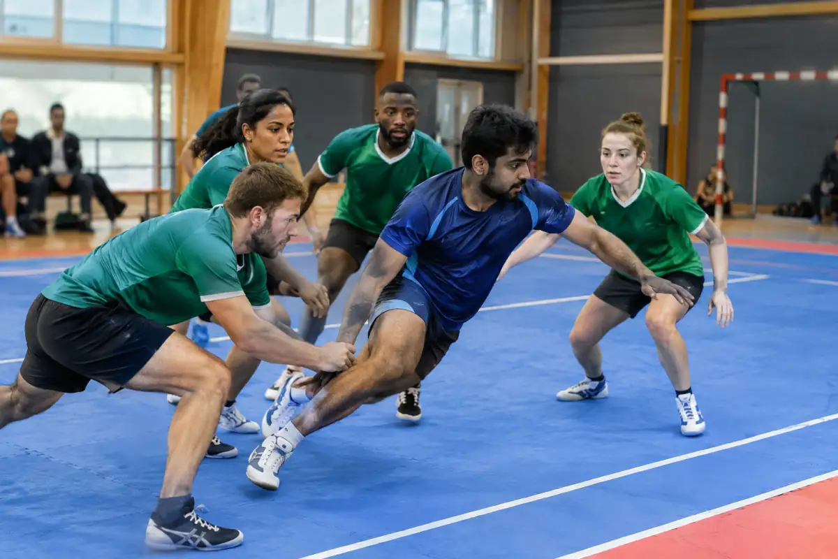 Un raider tente de toucher un défenseur sur un terrain rectangulaire pendant un match de kabaddi en salle.