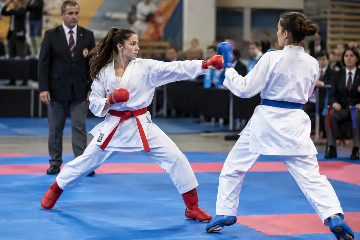 Échange de kumite au karaté : un pratiquant exécute un coup de poing contrôlé au corps sous le regard des arbitres.