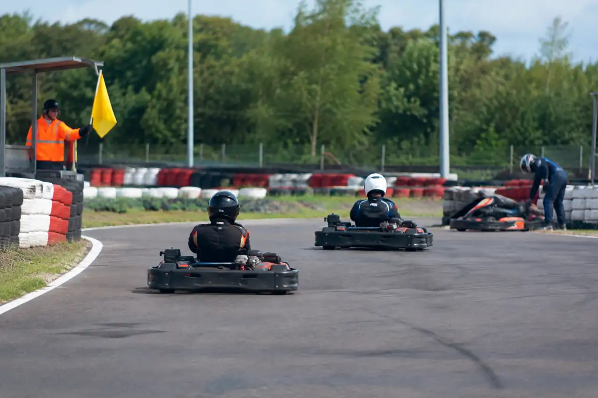 Un commissaire agite un drapeau jaune devant des karts qui ralentissent et gardent leur trajectoire sur le circuit.