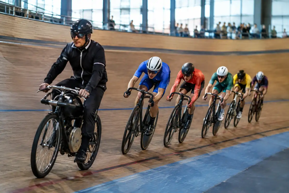 Des coureurs à vélo de piste suivent un entraîneur motorisé sur un vélodrome pendant une course de keirin.