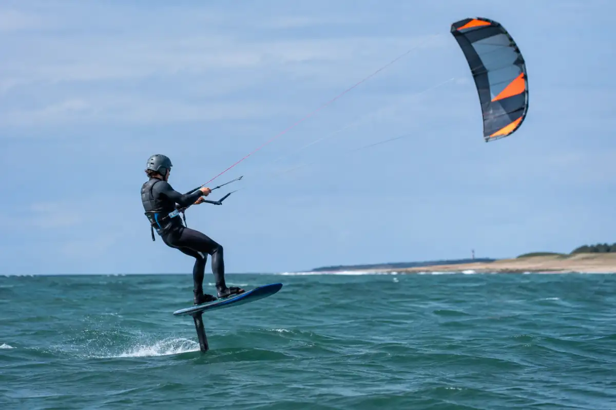 Un pratiquant de kitefoil en combinaison glisse au-dessus de l’eau, tracté par son aile et porté par le foil.