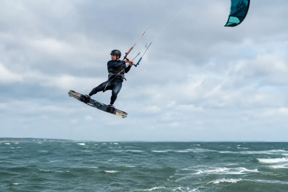 Un pratiquant de kitesurf big air réalise un saut au-dessus de l’eau, équipé d’une planche twin-tip et de protections.
