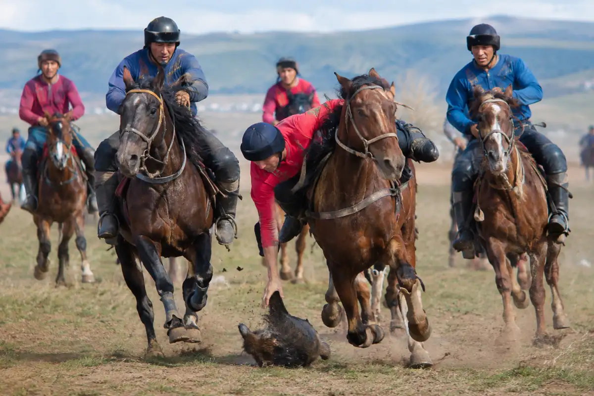 Des cavaliers disputent la carcasse au sol pendant une partie de kokpar sur un vaste terrain extérieur au Kazakhstan.