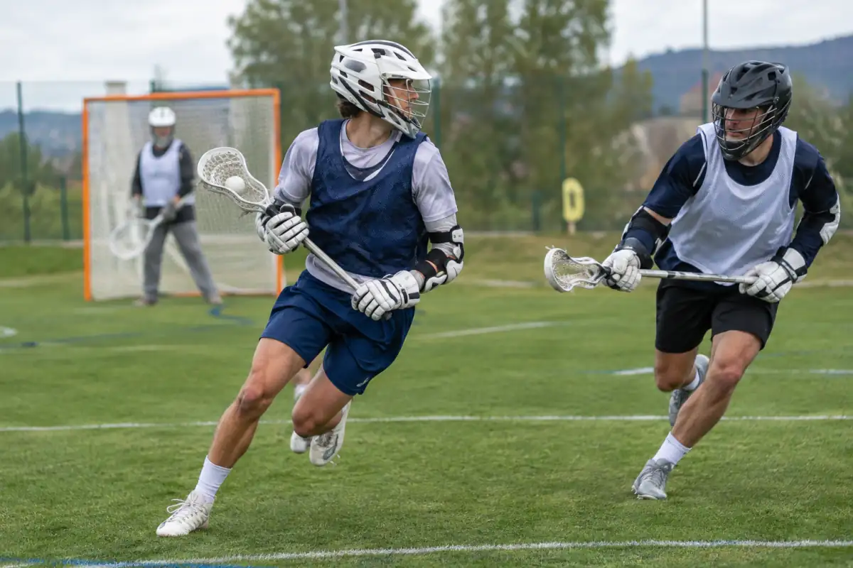 Joueur de lacrosse en champ portant la balle dans sa crosse pendant qu’un défenseur tente de fermer l’angle de tir.