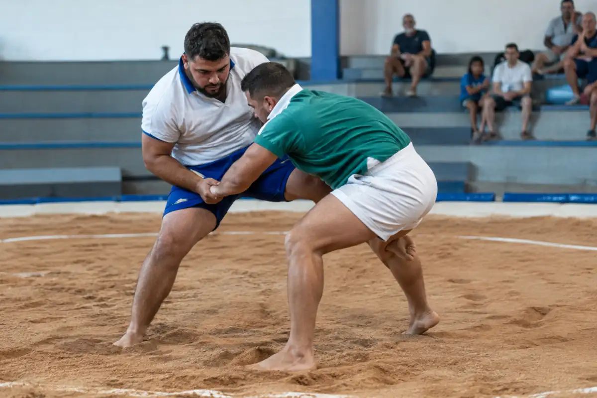 Deux lutteurs pieds nus s’affrontent dans un terrero lors d’un combat de lucha canaria, en tentant un déséquilibre contrôlé.