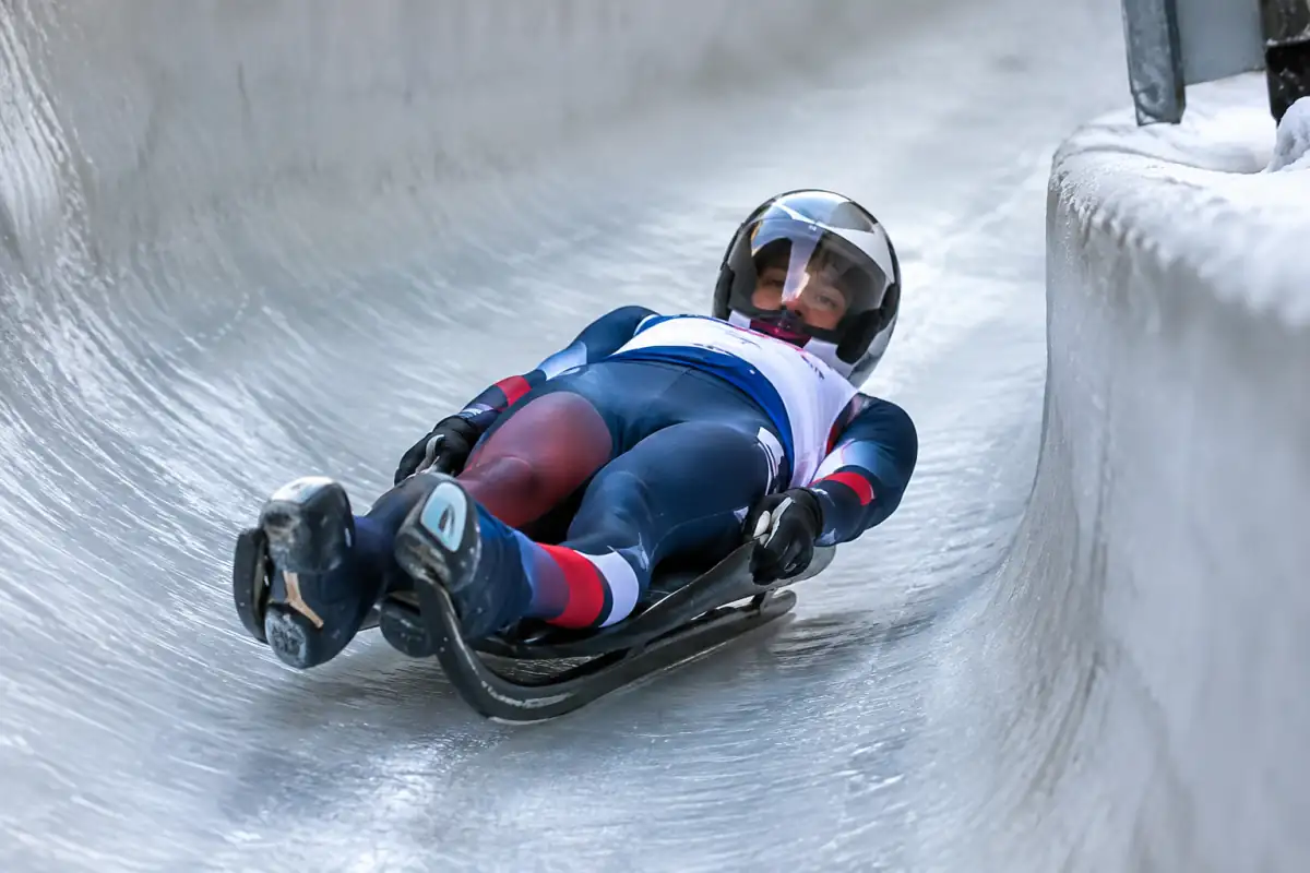 Athlète en luge sportive, allongé sur le dos et pieds en avant, négociant un virage sur une piste glacée.