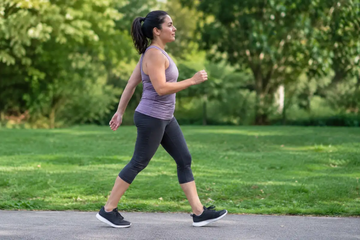 Marcheuse en profil sur un chemin plat, buste droit, bras détendus et pas courts pour accélérer sans courir.