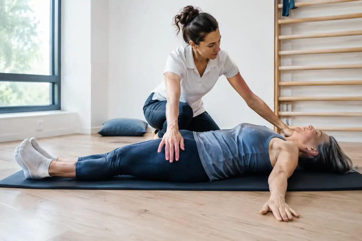 Séance de méthode Mézières : un kinésithérapeute accompagne une personne dans une posture d’étirement au sol.