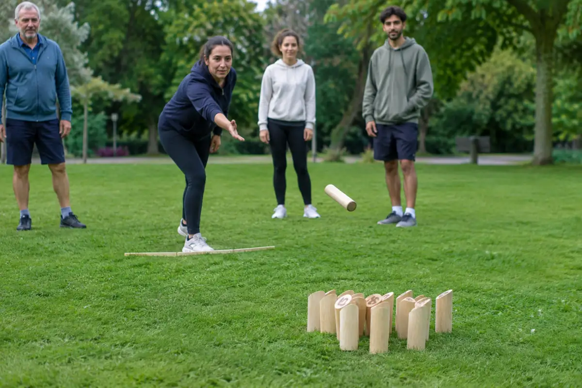 Une joueuse lance le bâton de Mölkky vers des quilles numérotées en bois sur une pelouse, sous le regard des autres participants.