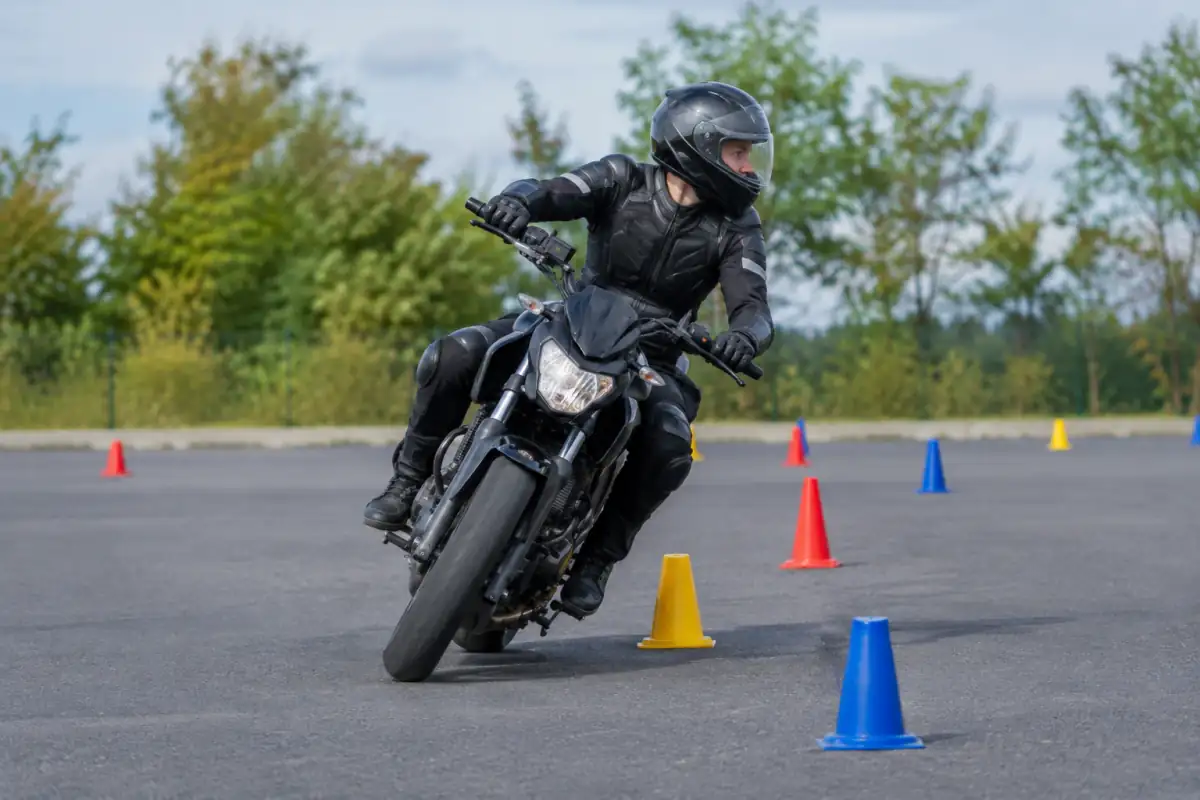 Pilote équipé négociant un slalom serré de cônes à moto sur une aire asphaltée lors d’une séance de moto gymkhana.