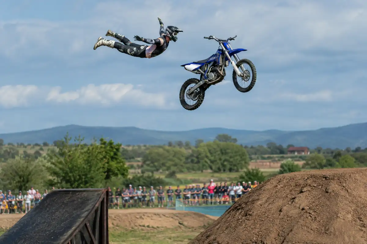 Un pilote de motocross freestyle réalise une figure aérienne au-dessus d’une réception aménagée, avec casque et protections.