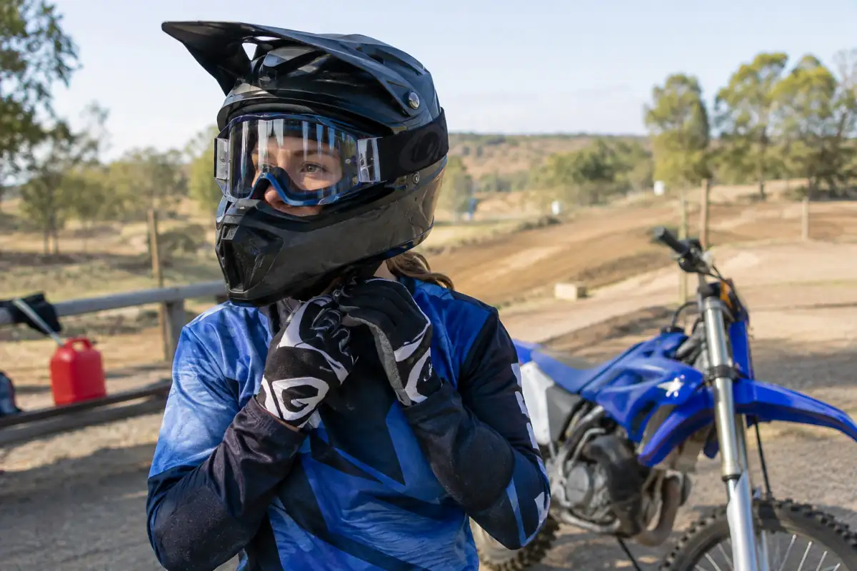 Un débutant vérifie l’ajustement de son casque et de ses lunettes de motocross près de sa moto avant une séance.