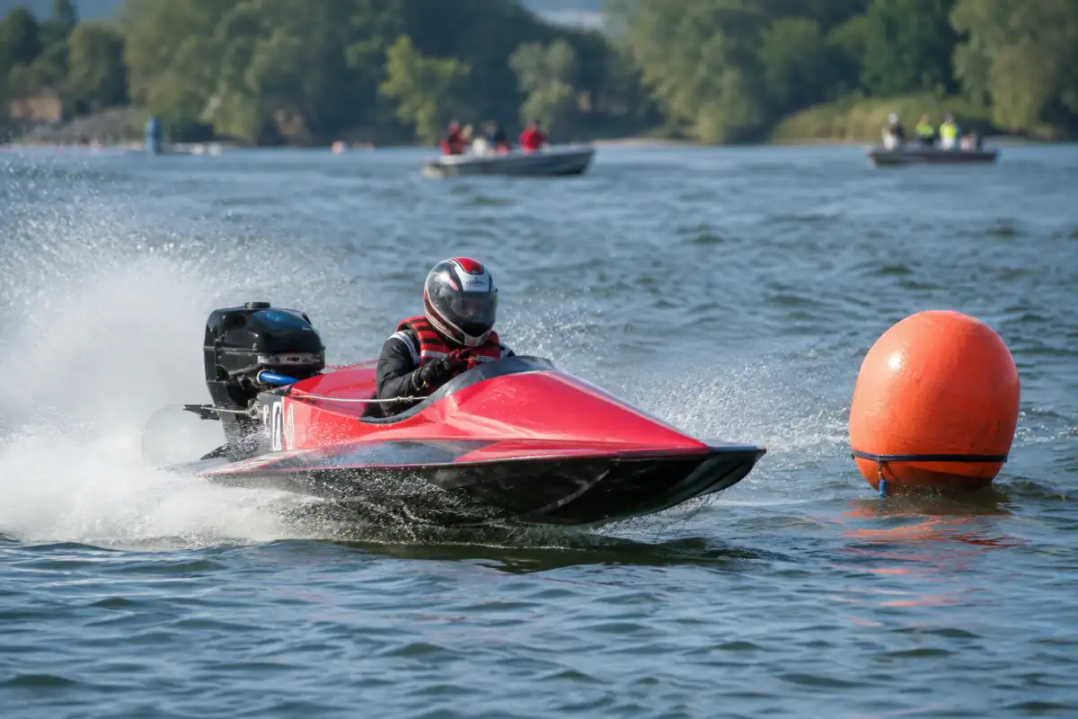 Un pilote casqué en bateau de course à moteur contourne une bouée sur un circuit balisé, sous la surveillance de bateaux de sécurité.