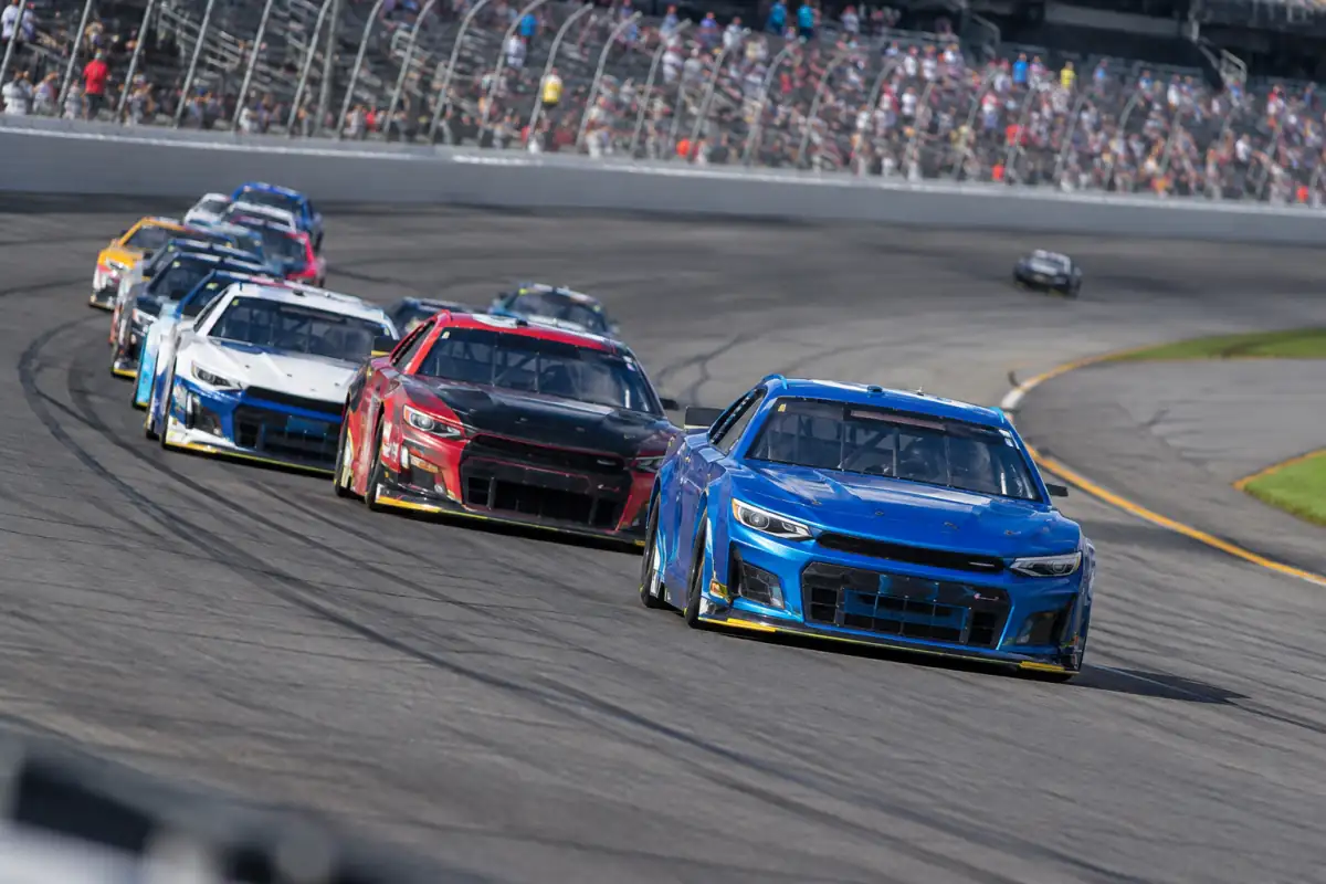 Peloton de voitures de stock-car en course dans un virage incliné d’un circuit ovale de NASCAR.