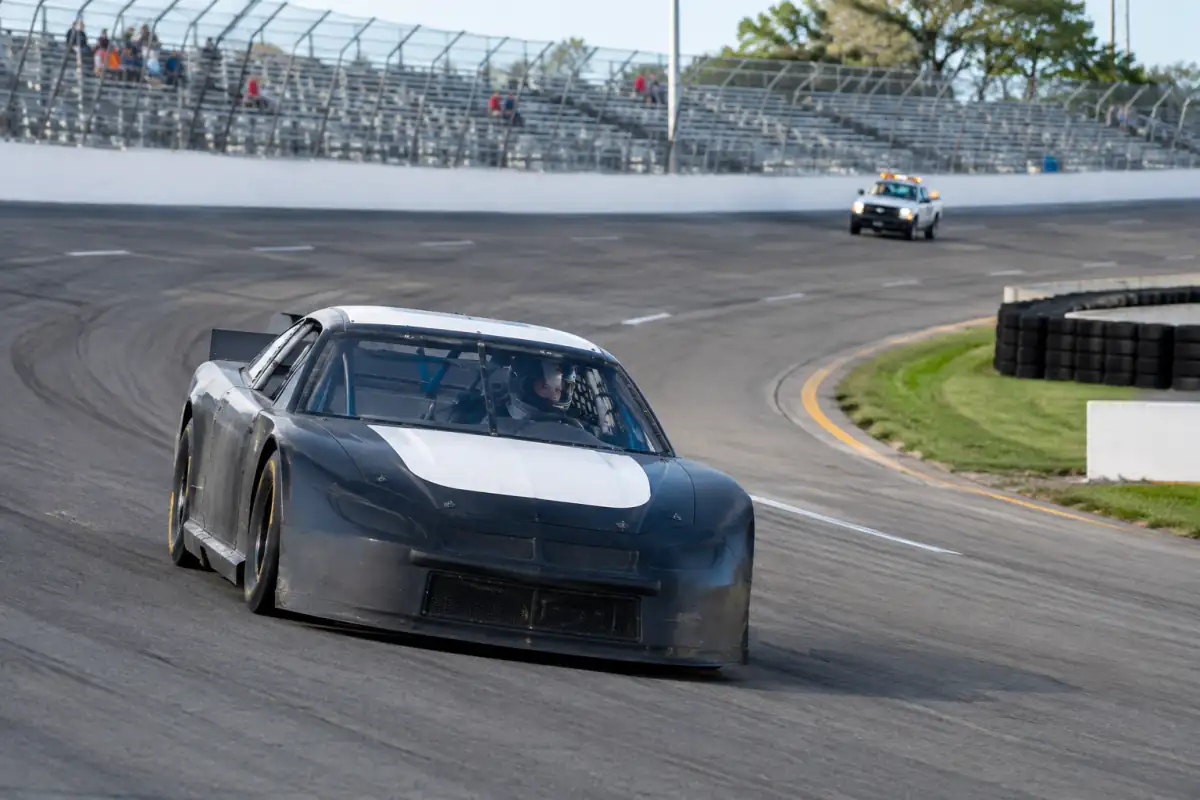 Stock-car à allure d’entraînement dans un virage incliné, le pilote regardant la sortie et maintenant une trajectoire régulière sur l’ovale.