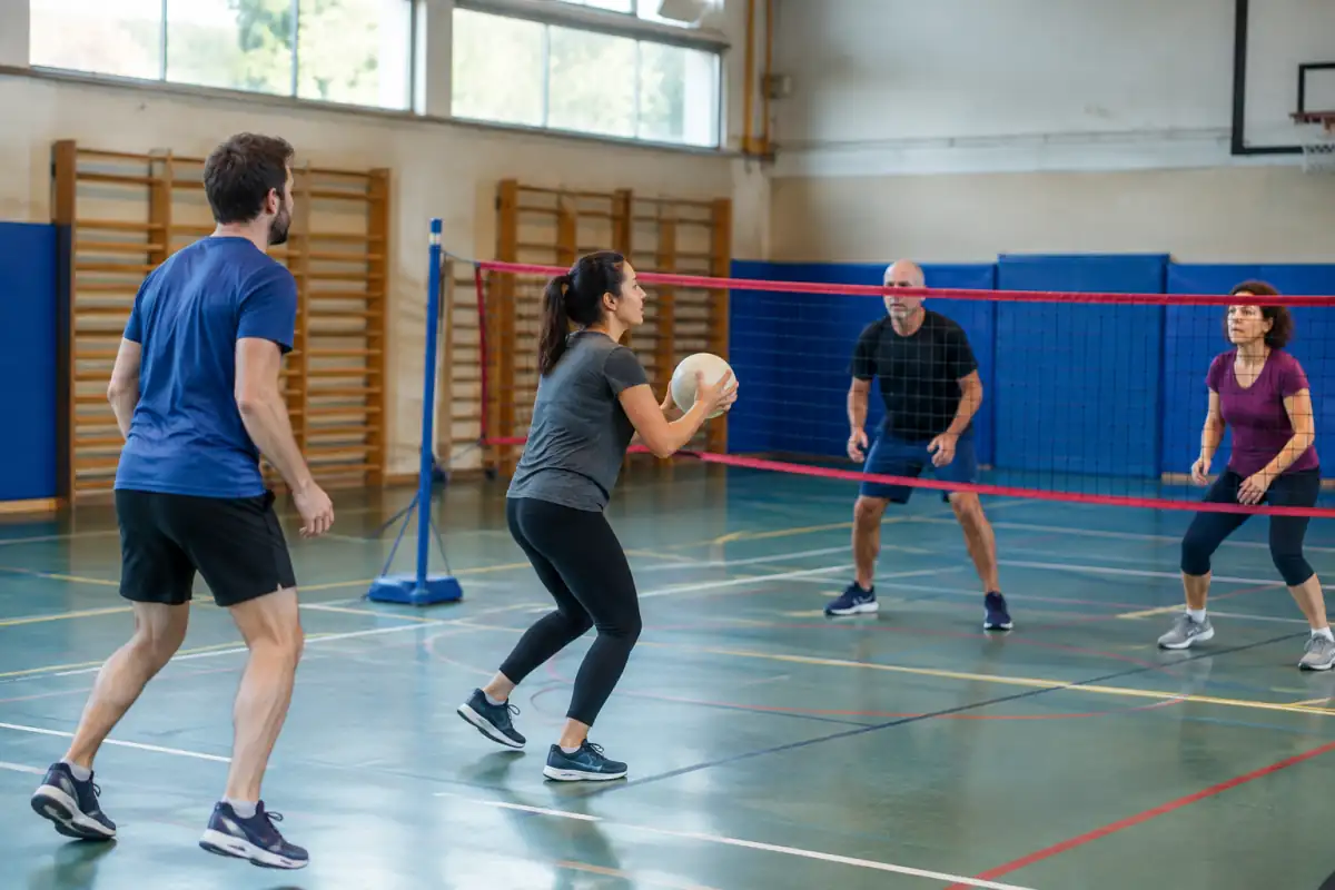 Des joueurs se préparent à attraper et lancer un ballon au-dessus du filet lors d’une partie de Newcomb-ball en gymnase.