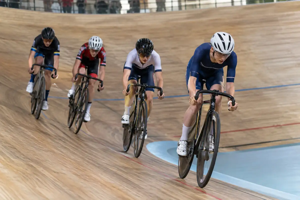 Coureurs disputant un omnium sur piste, en vélos à pignon fixe, dans les virages relevés d’un vélodrome couvert.
