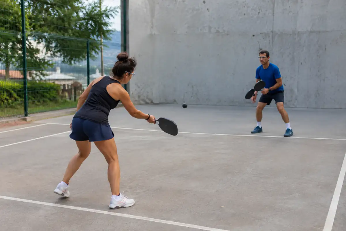 Partie de paddleball mural : deux joueurs munis de palettes rigides et de lunettes échangent une balle sur un terrain extérieur.